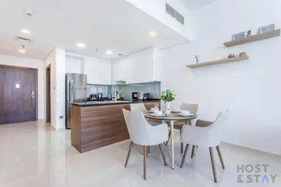 a kitchen with a table and white chairs at Lively 1 BR in Damac Hills, Dubai - Host & Stay in Dubai