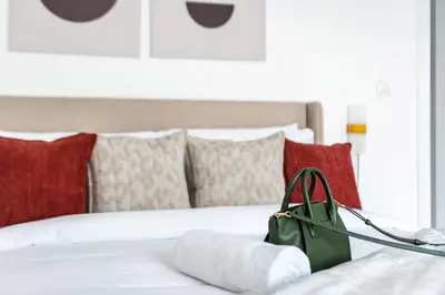 a green purse sitting on a bed with red pillows at Stella Stays Lana Tower in Dubai