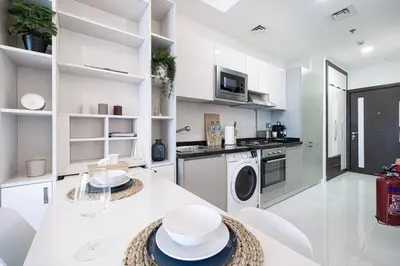 a white kitchen with a table and white appliances at Nice studio in Arjan - Dubai in Dubai
