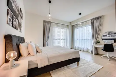 a bedroom with a bed and a desk and windows at 2BD apartment near the beach in Bahar, JBR in Dubai
