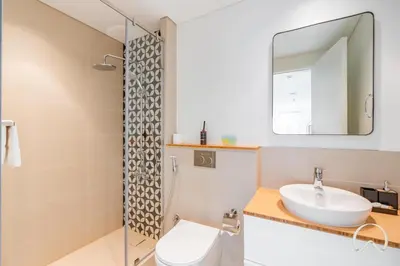 a bathroom with a sink and a toilet and a mirror at Oraya - Stylish 2BR in Socio Tower 2 With Pool View in Dubai