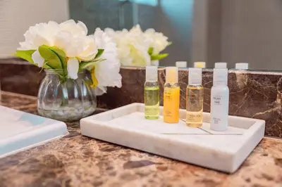 a counter with three bottles on a tray with flowers at Prime Retreats - Sparkle Tower Marina in Dubai