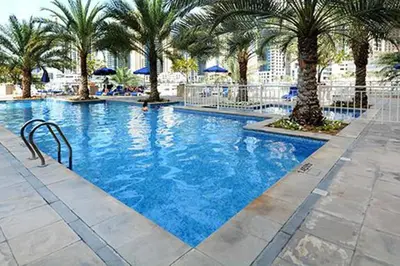 a large swimming pool with palm trees and blue umbrellas at Dubai Marina Walking distance to metro Marina View in Dubai