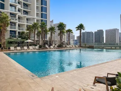a large swimming pool with palm trees and buildings at ALiving Chic Studio Apartment I Partial Burj Khalifa & Canal View I DAMAC Maison Prive B- 1417 in Dubai