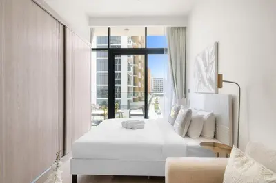 a bedroom with a white bed and a large window at Lovely Studio with Gym, Pool and BBQ Facilities in Dubai