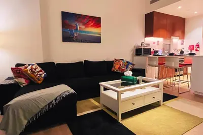 a living room with a black couch and a kitchen at Full Seaview Comfortable Apt La Mer Dubai in Dubai