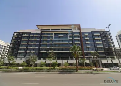 a large building with palm trees in front of a street at Attractive Studio Apartment in Azizi Riviera 15, Al Merkadh by Deluxe Holiday Homes in Dubai