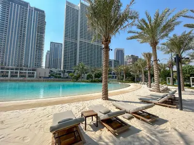 a beach with chaise lounges and a pool with palm trees at Elegant at Creek Beach 1 BHK in Dubai