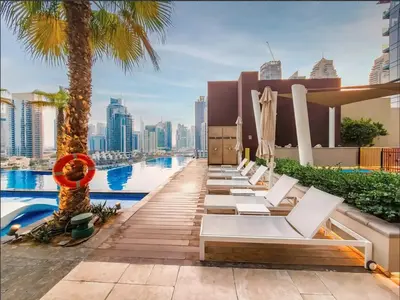 a row of white lounge chairs on the roof of a building with a pool at Chic 1-Bed Near Marina Promenade - 5 min to Tram in Dubai