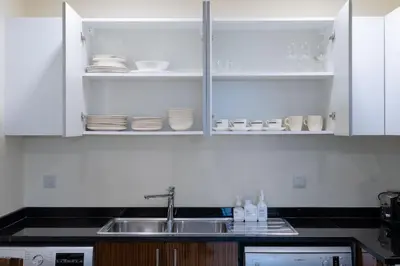 a kitchen with white cabinets and a sink and dishes at Dubai Modern Apartment l Sleeps 4 l 2 Baths in Dubai