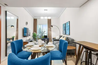 a living room with a table and blue chairs at StoneTree - Cozy 1 BR - Near Metro in Dubai
