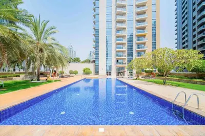 a large swimming pool with palm trees and a tall building at Marina Tower - Stunning 1BHK with Marina View by Elegant Escape's in Dubai