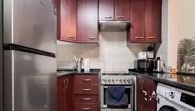 a kitchen with wooden cabinets and a stainless steel refrigerator at Rare Holiday Homes - Mediterranean Cluster - Near Ibn Battuta Mall - Discovery Garden - Building# Med 49 - R106 in Dubai