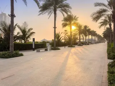 a walkway with palm trees and the sun setting at Five Palm Luxury - 2BR with Pool View, Gym & Prime Beach Stay in Dubai