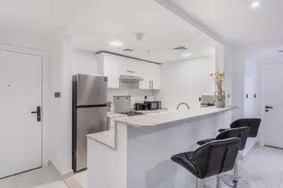 a white kitchen with a refrigerator and black chairs at Comfy 1BR Marina Living Steps from Marina Walk in Dubai