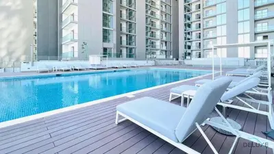 a swimming pool with two lounge chairs next to a building at Charming 1BR Apartment in Sobha Creek Vistas Reserve, Al Merkadh by Deluxe Holiday Homes in Dubai
