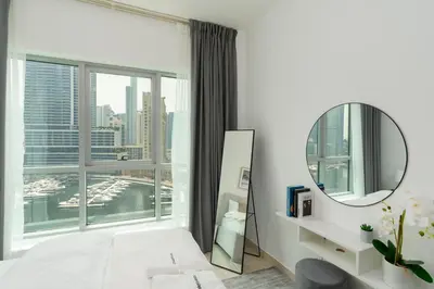 a white bedroom with a mirror and a large window at Gala Guests - Stunning Front-Row Marina Views at The Point in Dubai