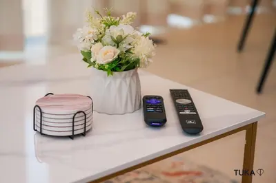 a table with a vase of flowers and two remote controls at Skyline & Lake views - Home Cinema - 1-BHK - Prime Location in Dubai