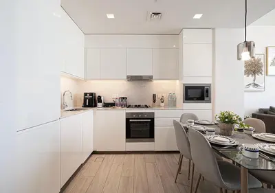 a kitchen with white cabinets and a table with chairs at Palace Residences 2BR with Stunning Creek Views in Dubai