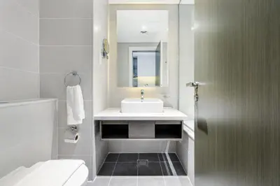 a white bathroom with a sink and a mirror at A Living-Modern Studio Apartment with Balcony & Canal view at Prive 2507B ,Business Bay in Dubai