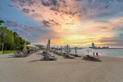 a beach with a bunch of chairs and umbrellas at Palm Paradise 1BR - Beachfront Escape with Pool, Gym, Parking & Balcony in Dubai