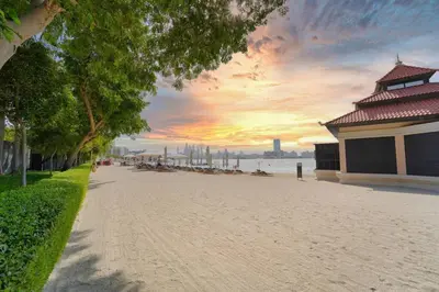a beach with a building and trees and a sunset at Palm Paradise 1BR - Beachfront Escape with Pool, Gym, Parking & Balcony in Dubai
