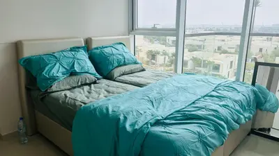 a bed with blue comforter in a room with a window at Damac Golf vita in Dubai