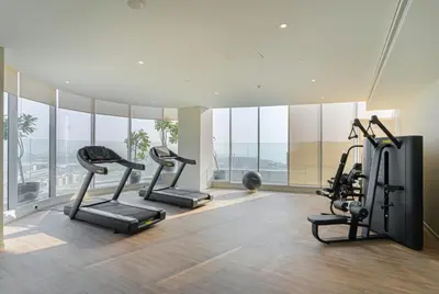a gym with treadmills and ellipticals in a room with windows at Savis Homes - Condor Marina Star - Luxury 2 BR Waterfront Apartment in Dubai