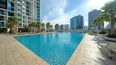 a large swimming pool with palm trees and buildings at Deluxe One-Bedroom Apartment in Business Bay with Burj Khalifa and Canal View in Dubai