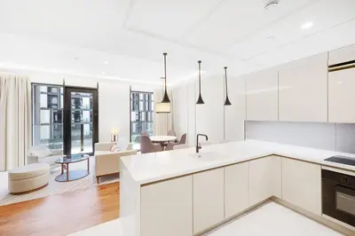 a kitchen with white cabinets and a living room at Vonder Bluewaters Residences SA2 in Dubai