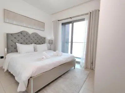 a white bedroom with a large bed and a window at Fast Wi-fi Netflix Cozy 1BR Flat Near Downtown Dubai in Dubai