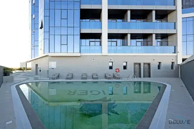 a building with a swimming pool in front of a building at Stylish Studio Apartment in Blue Wave Tower, Dubailand by Deluxe Holiday Homes in Dubai