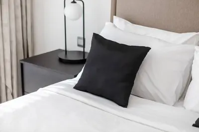 a bed with a black pillow and white pillows at Spacious 1 BR Lagoon in Dubai