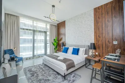 a bedroom with a bed with blue pillows and a desk at Escape24 Premium Studio in Damac Hills in Dubai