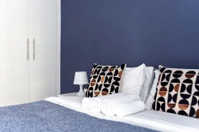 a white bed with pillows and a blue wall at ShoresInn - Elegant 2BR with Dubai Marina View in Dubai