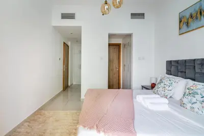 a white bedroom with a large bed with a pink blanket at ShoresInn - Chic Waterfront Living in Dubai Marina in Dubai