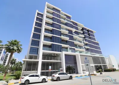 two cars parked in front of a large building at Premium 1BR at DAMAC Hills Loreto 1B in Dubailand by Deluxe Holiday Homes in Dubai