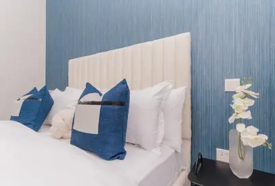 a bed with blue and white pillows and a vase with flowers at Classy 1BR Midtown Stay Near Miracle Garden by Vibel in Dubai