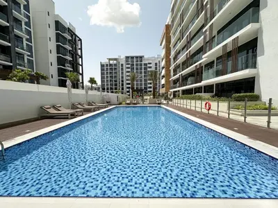 a large swimming pool with chairs and buildings at Trophy Blissful Bend Studio in Meydan with Pool Views in Dubai