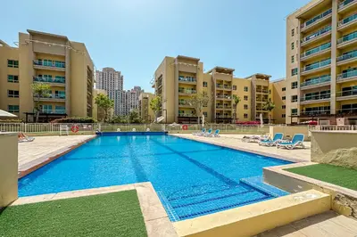 a large swimming pool with chairs and buildings at 1BR The Greens Courtyard View in Dubai