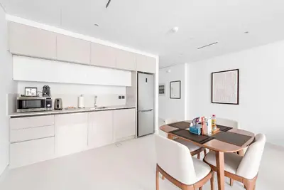 a kitchen with white cabinets and a wooden table and chairs at Silkhaus Marina View 1BDR Private Beach Access in Dubai