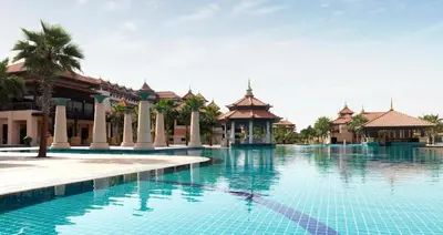 a pool at a resort with palm trees and buildings at Luxury Holiday Home, Spacious 1 bedroom, Burj Alarab full ocean view, located in Anantara the palm, Palm Jumeirah, Dubai in Dubai