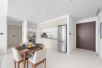 a white kitchen with a wooden table and chairs at Silkhaus 1BDR with Private Beach Marina Vista in Dubai