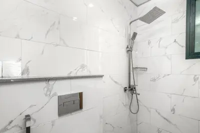 a white tiled shower with a shower head in a bathroom at Cozy Studio - Dubai Land -Tiger V Tower in Dubai