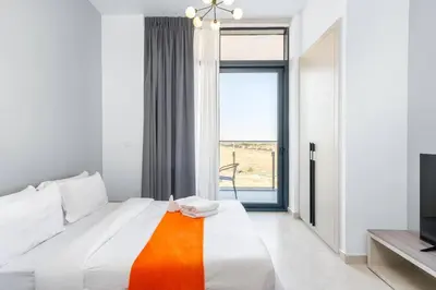 a white bedroom with a large bed and a television at Cozy Studio - Dubai Land -Tiger V Tower in Dubai