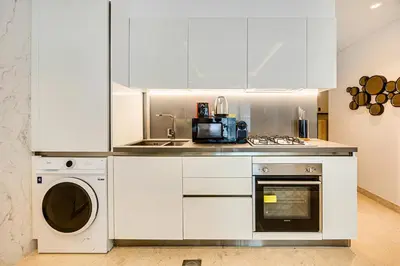 a white kitchen with a sink and a dishwasher at Cute studio in The Sterling by Omniyat in Dubai
