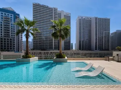 a swimming pool with two chairs and palm trees on a building at Cute studio in The Sterling by Omniyat in Dubai