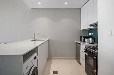 a white kitchen with a sink and a dishwasher at Bright Studio In Vibrant Dubailand District in Dubai