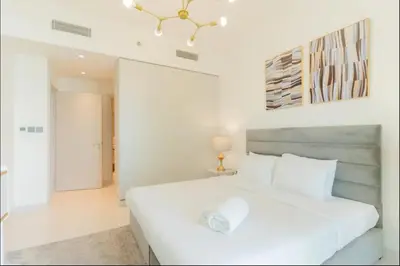 a white bedroom with a white bed and a chandelier at AWS Holiday Homes - Memories by the Beach in Dubai