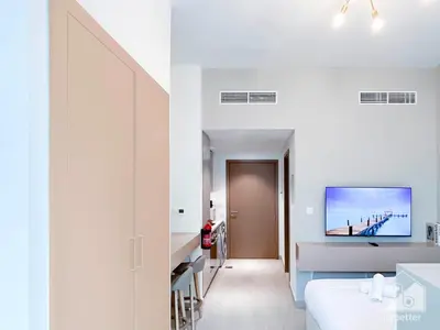a white room with a bed and a tv on the wall at Cozy Studio with Balcony & Stunning Views in Dubai